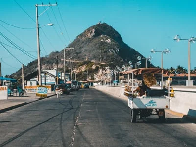 image depicts a street in Mexico with a mountain in the distance.