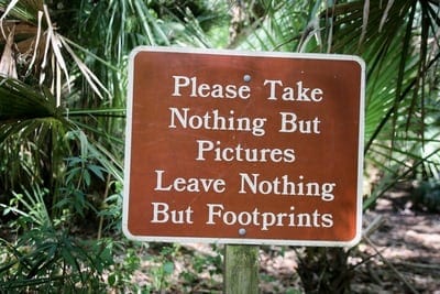 image depicts a sign which says "Please take nothing but flowers. Leave nothing but footprints."