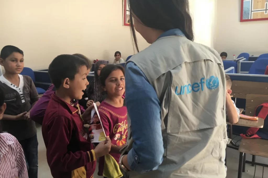image depicts a Unicef volunteer standing in front of children