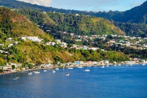 Image shows the hilly, tropical island of Dominica, with ocean in the foreground