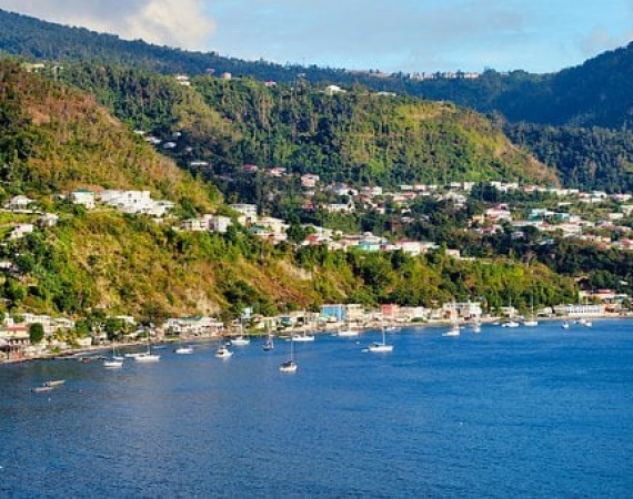 Image shows the hilly, tropical island of Dominica, with ocean in the foreground